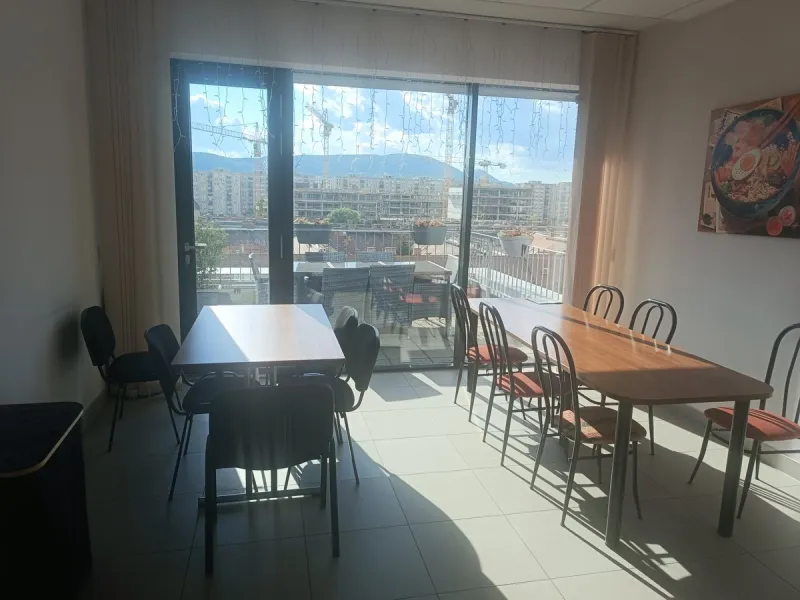 Phone photo of an office canteen with long tables and glass doors to a roof terrace, shot against the light