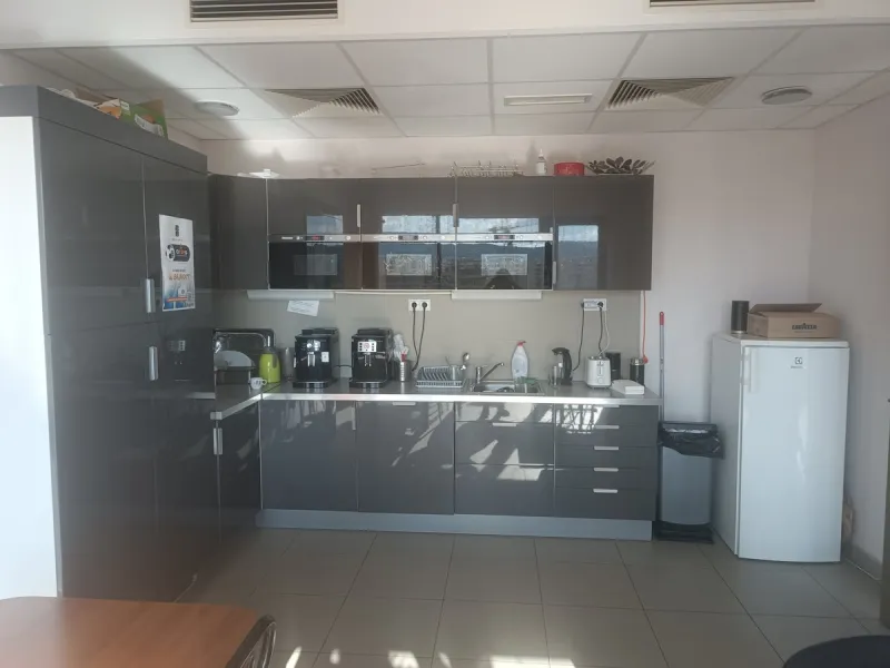 Phone photo of an office kitchen with dark grey cabinets, coffee machines, a mini fridge and dishes by the sink